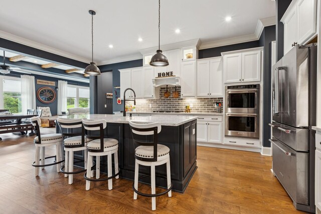 6013 Blackwell Ln, Franklin, TN 37064 - kitchen with appliances with stainless steel finishes, crown molding, white cabinetry, a breakfast bar, and decorative backsplash