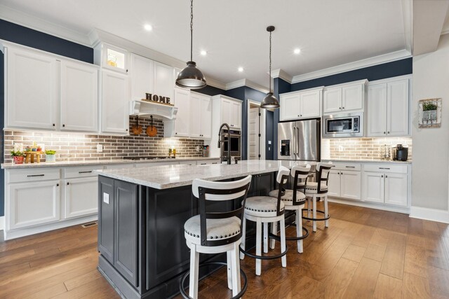 6013 Blackwell Ln, Franklin, TN 37064 - kitchen featuring appliances with stainless steel finishes, tasteful backsplash, an island with sink, white cabinetry, and ornamental molding