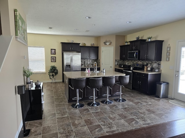 1736 Bellamy Ln, Murfreesboro, TN 37128 - kitchen with appliances with stainless steel finishes, backsplash, a center island with sink, a kitchen bar, and a textured ceiling