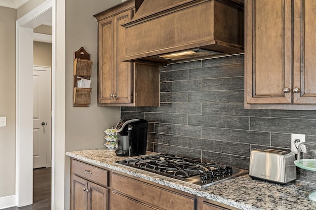 318 Finnhorse Ln, Franklin, TN 37064 - kitchen with premium range hood, stainless steel gas stovetop, backsplash, brown cabinets, and light stone counters