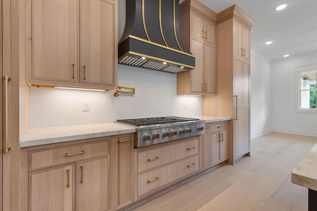 7312 Walker Rd, Fairview, TN 37062 - kitchen with light brown cabinetry, stainless steel gas stovetop, wall chimney exhaust hood, light wood finished floors, and light stone countertops