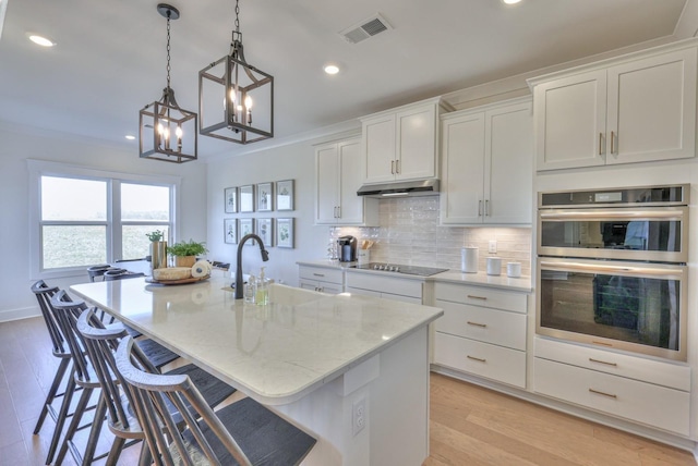2816 Kai Dr, Murfreesboro, TN 37129 - kitchen featuring black electric stovetop, double oven, under cabinet range hood, a center island with sink, and light wood finished floors
