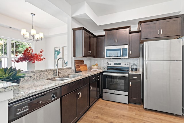 1108 Somerset Springs Dr, Spring Hill, TN 37174 - kitchen featuring appliances with stainless steel finishes, light stone countertops, dark brown cabinets, a chandelier, and light wood finished floors
