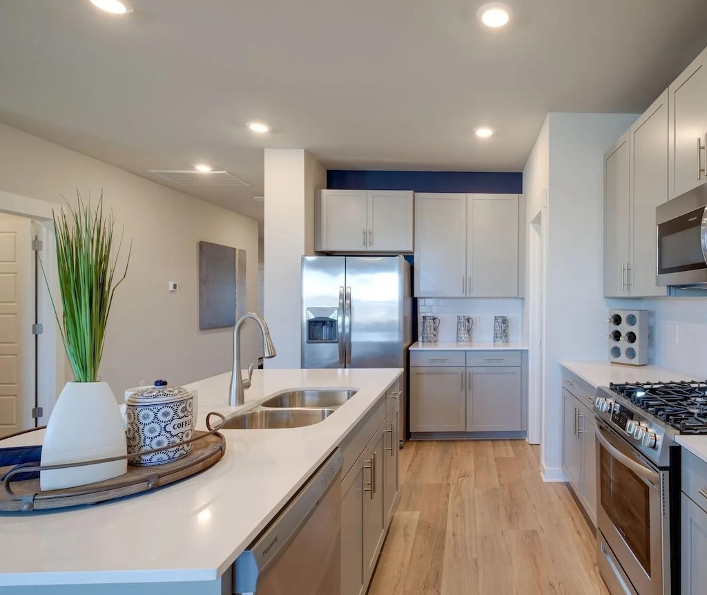 140 Ravens Crest Ave, Mount Juliet, TN 37122 - kitchen with stainless steel appliances, a kitchen island with sink, light wood finished floors, light countertops, and tasteful backsplash