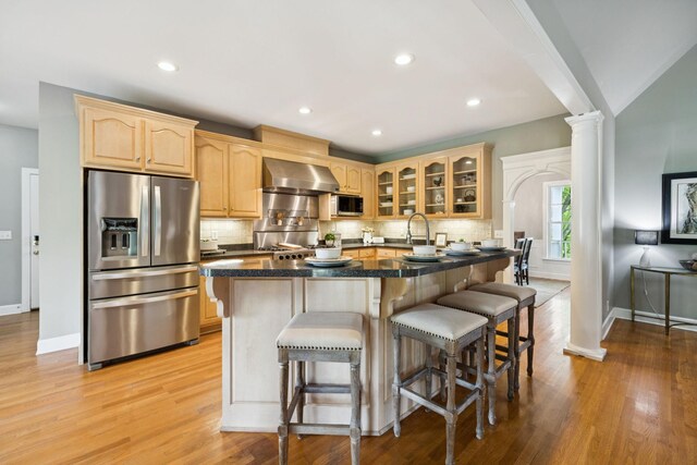 1387 Floyd Rd, Eagleville, TN 37060 - kitchen with appliances with stainless steel finishes, wall chimney range hood, decorative columns, glass insert cabinets, and light brown cabinets