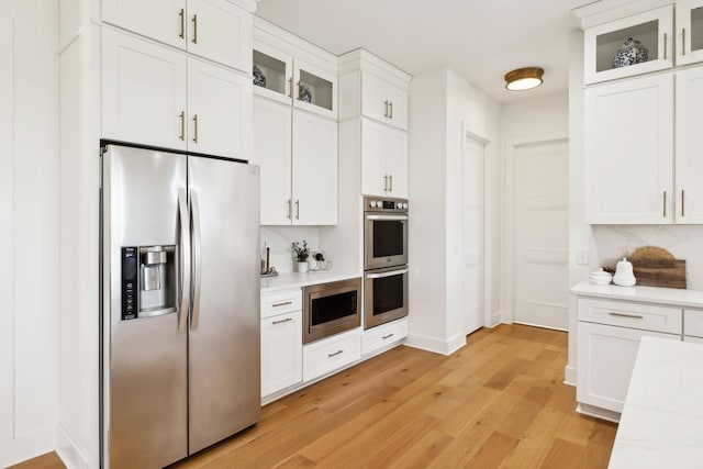 973 Hall Cemetery Rd, Burns, TN 37029 - kitchen with stainless steel appliances, light wood-style floors, white cabinets, tasteful backsplash, and glass insert cabinets