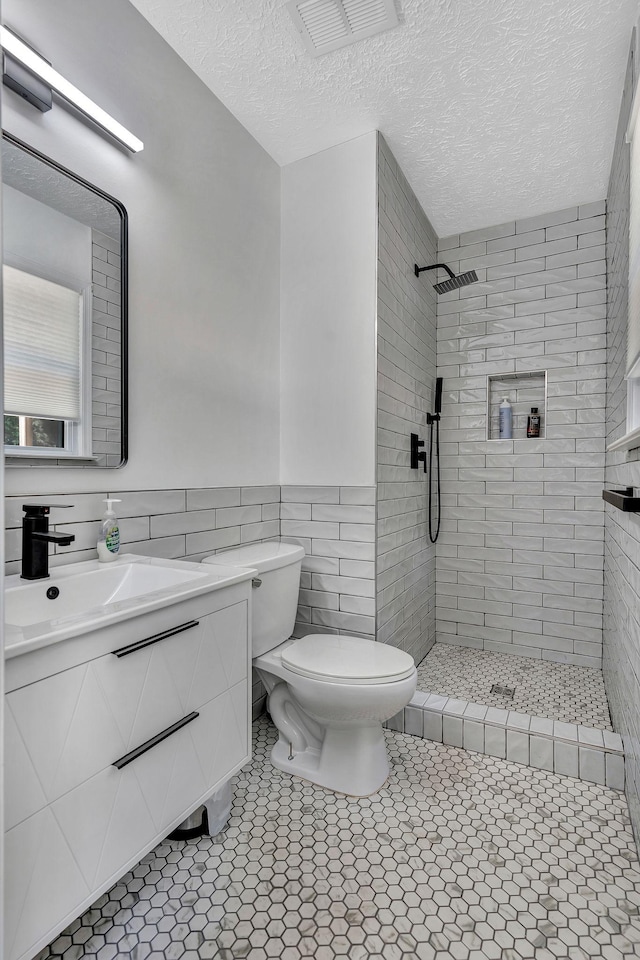 141 Springbrook Pl, Joelton, TN 37080 - bathroom featuring tiled shower, vanity, tile walls, wainscoting, and a textured ceiling