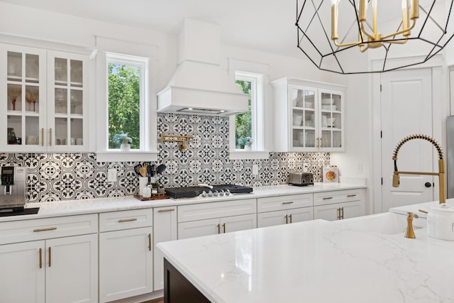 5128 Terravista Ln, Franklin, TN 37064 - kitchen featuring premium range hood, stainless steel gas cooktop, white cabinetry, backsplash, and glass insert cabinets
