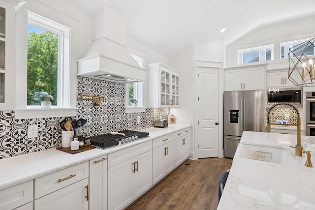 5128 Terravista Ln, Franklin, TN 37064 - kitchen featuring appliances with stainless steel finishes, premium range hood, lofted ceiling, glass insert cabinets, and white cabinetry