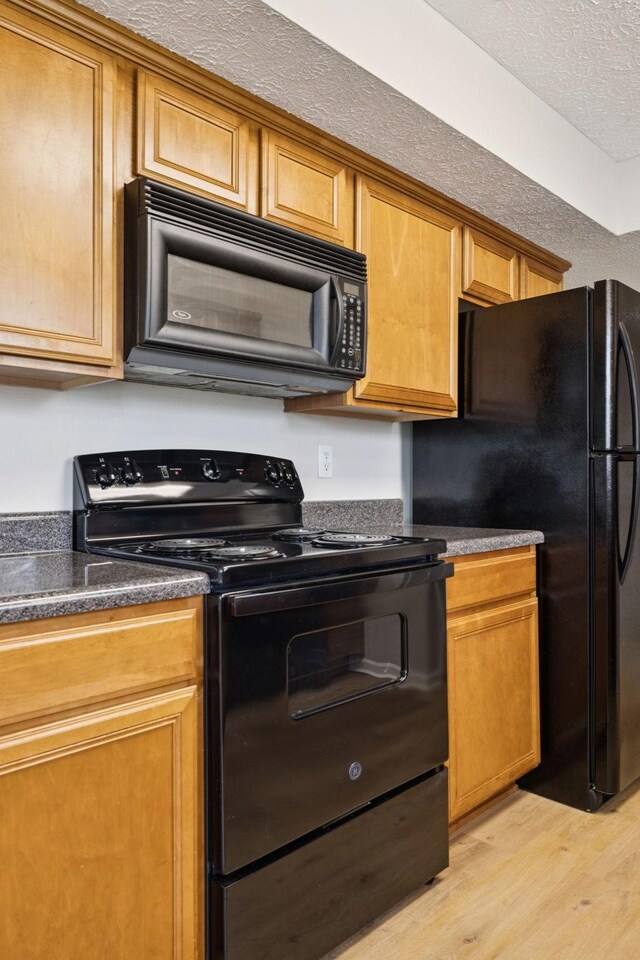 1882 Portway Rd, Spring Hill, TN 37174 - kitchen with black appliances, light wood finished floors, dark countertops, a textured ceiling, and brown cabinets