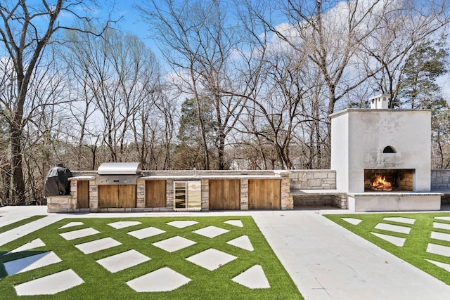 6128 Lookaway Cir, Franklin, TN 37067 - view of grassy yard featuring a warm lit fireplace, exterior kitchen, wine cooler, and view of wooded area