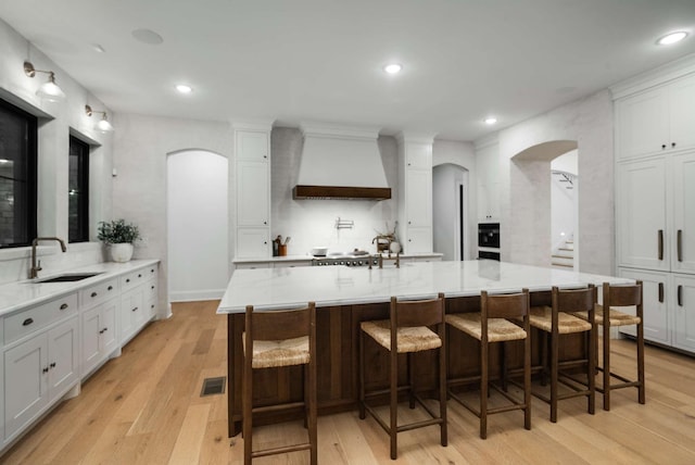 6128 Lookaway Cir, Franklin, TN 37067 - kitchen with custom range hood, arched walkways, light wood finished floors, white cabinetry, and recessed lighting