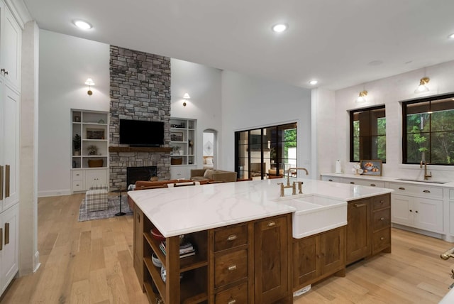 6128 Lookaway Cir, Franklin, TN 37067 - kitchen with light wood finished floors, white cabinets, a fireplace, open shelves, and a center island with sink