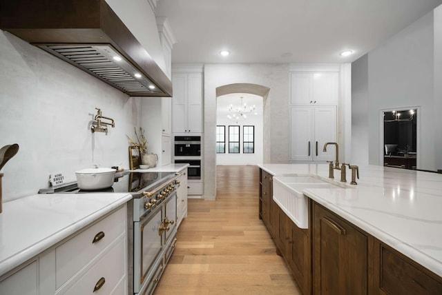 6128 Lookaway Cir, Franklin, TN 37067 - kitchen featuring custom exhaust hood, stainless steel range, a chandelier, light wood finished floors, and white cabinetry