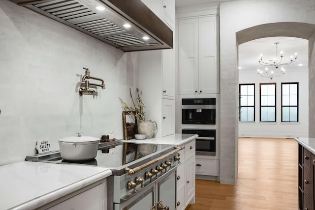 6128 Lookaway Cir, Franklin, TN 37067 - kitchen featuring wall chimney range hood, stove, arched walkways, light wood-style floors, and light countertops