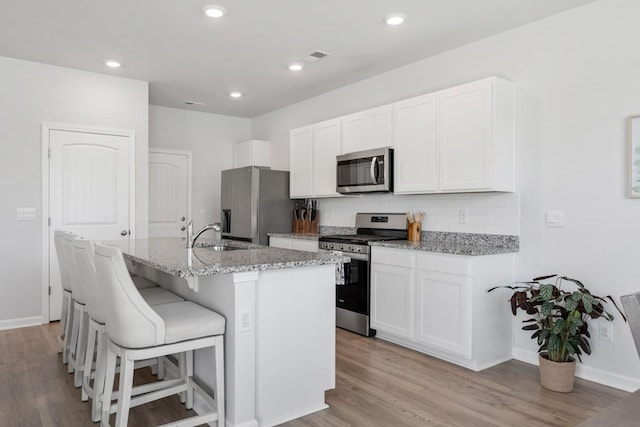 2400 Kaycee Ct, Lebanon, TN 37087 - kitchen featuring stainless steel appliances, an island with sink, light wood-type flooring, light stone counters, and backsplash