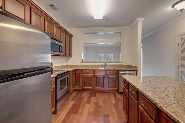 301 Criddle St Unit 304, Nashville, TN 37219 - kitchen featuring stainless steel appliances, light wood-style floors, crown molding, light stone countertops, and brown cabinets