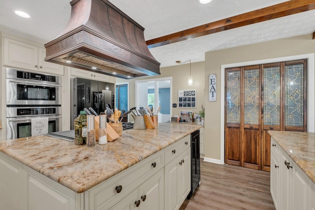 2600 Clanton Rd, Lawrenceburg, TN 38464 - kitchen with custom exhaust hood, stainless steel double oven, wine cooler, light stone countertops, and light wood-style floors