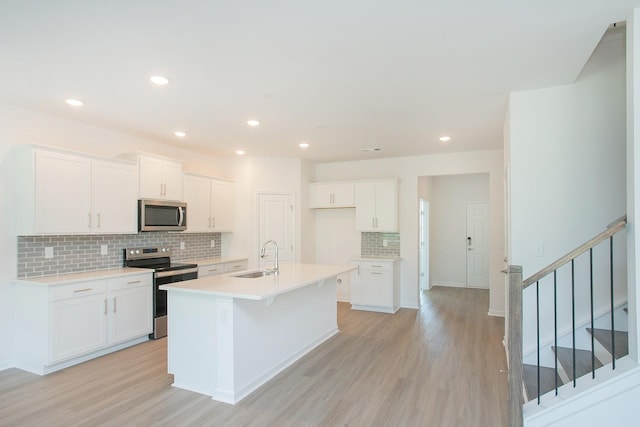 458 Jet Stream Dr, La Vergne, TN 37086 - kitchen with stainless steel appliances, decorative backsplash, light wood-style floors, white cabinets, and a center island with sink