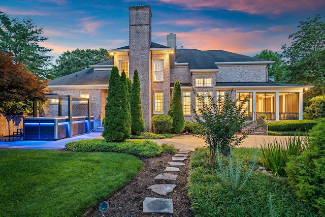 2455 Hidden River Ln, Franklin, TN 37069 - back of property at dusk with a chimney, brick siding, a patio area, a jacuzzi, and a yard