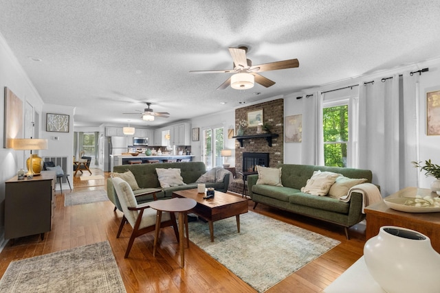 1830 Bradbury Rd, Adams, TN 37010 - living area featuring a textured ceiling, a ceiling fan, a brick fireplace, and light wood-style floors