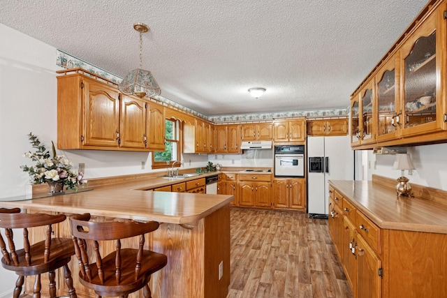 8663 Dog Branch Rd, Mount Pleasant, TN 38474 - kitchen featuring white appliances, under cabinet range hood, a peninsula, brown cabinets, and light wood-type flooring