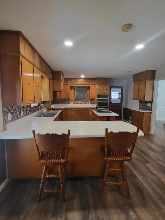 233 W Chestnut St, Puryear, TN 38251 - kitchen with a peninsula, dark wood-style flooring, brown cabinetry, backsplash, and light countertops