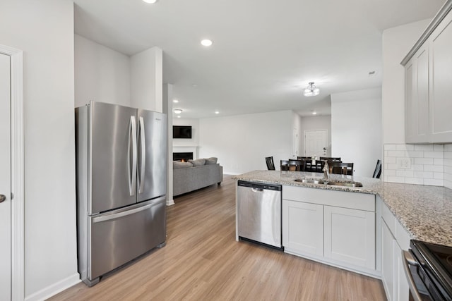 3276 Holiday Ln, Columbia, TN 38401 - kitchen with appliances with stainless steel finishes, a lit fireplace, a peninsula, light wood-type flooring, and light stone countertops