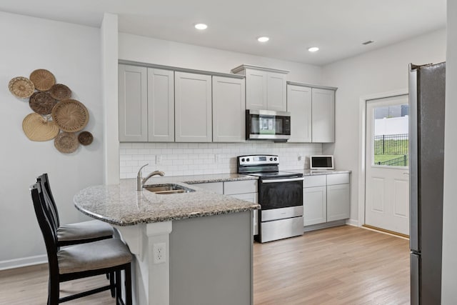 3276 Holiday Ln, Columbia, TN 38401 - kitchen featuring appliances with stainless steel finishes, a peninsula, light wood-type flooring, a breakfast bar area, and decorative backsplash