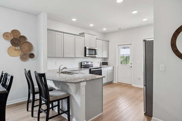 3276 Holiday Ln, Columbia, TN 38401 - kitchen with stainless steel appliances, backsplash, light stone counters, a breakfast bar area, and light wood-style floors