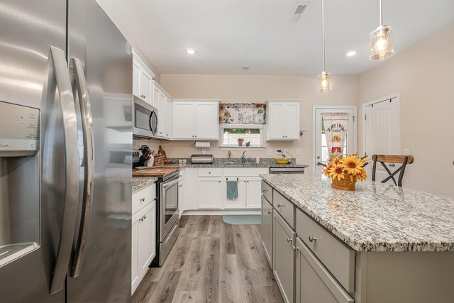 523 Moshe Flam Pl, La Vergne, TN 37086 - kitchen featuring appliances with stainless steel finishes, light wood-style floors, a center island, decorative light fixtures, and white cabinetry