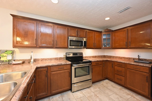 395 Devon Chase Hl Unit 3602, Gallatin, TN 37066 - kitchen featuring appliances with stainless steel finishes, glass insert cabinets, a textured ceiling, brown cabinetry, and recessed lighting