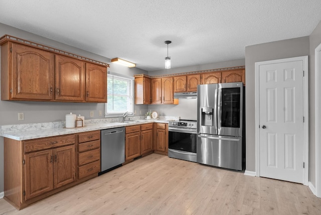 2430 Underwood Rd, Cunningham, TN 37052 - kitchen with appliances with stainless steel finishes, brown cabinets, light wood-style flooring, under cabinet range hood, and light countertops