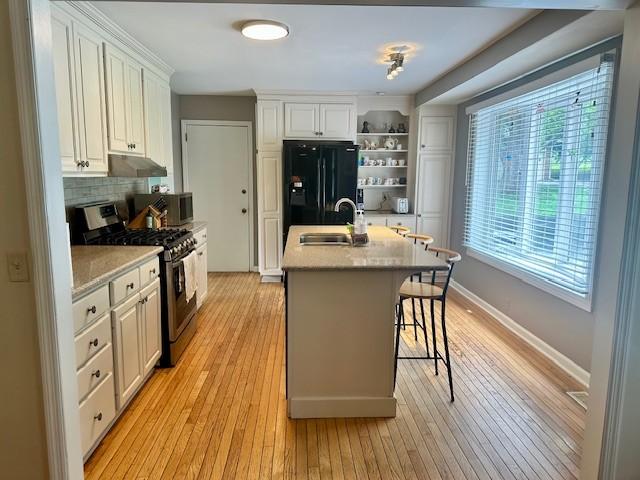 303 Revere Ln, Franklin, TN 37064 - kitchen featuring appliances with stainless steel finishes, open shelves, light wood-style flooring, and a breakfast bar area