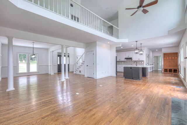 1202 Willow Brook Pass, Mount Juliet, TN 37122 - unfurnished living room with light wood-style floors, a ceiling fan, a towering ceiling, and decorative columns