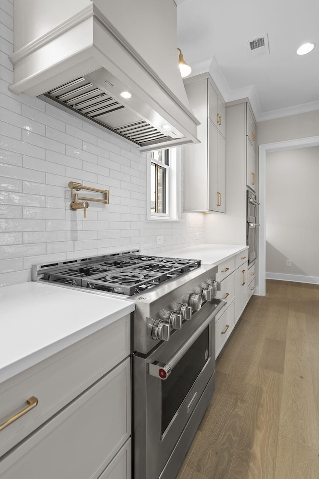 8011 Cane Creek Rd, Nashville, TN 37221 - kitchen with stainless steel stove, premium range hood, backsplash, light countertops, and wood finished floors
