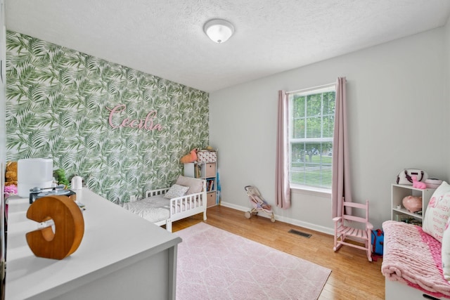 113 Beck Ct, Murfreesboro, TN 37128 - bedroom featuring light wood finished floors, wallpapered walls, a textured ceiling, and an accent wall