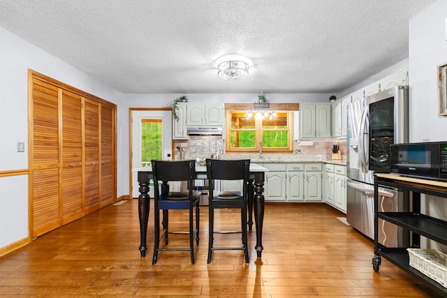 5719 Minor Hill Hwy, Goodspring, TN 38460 - kitchen with under cabinet range hood, backsplash, black microwave, light wood-type flooring, and a textured ceiling