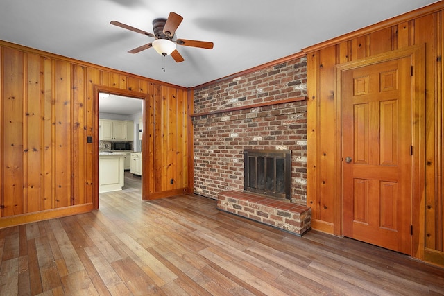 2411 Woolson Rd, Chattanooga, TN 37406 - unfurnished living room featuring a ceiling fan, wooden walls, a brick fireplace, wood finished floors, and crown molding