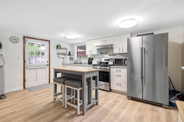 1795 Lake Logan Rd, Ardmore, TN 38449 - kitchen with appliances with stainless steel finishes, under cabinet range hood, stacked washer / drying machine, light wood finished floors, and white cabinetry