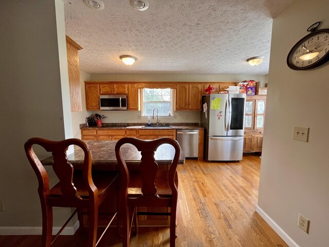 4038 Mount Zion Rd, Morrison, TN 37357 - kitchen with stainless steel appliances, brown cabinetry, light wood-type flooring, a textured ceiling, and dark countertops