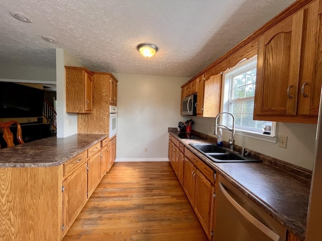 4038 Mount Zion Rd, Morrison, TN 37357 - kitchen with stainless steel appliances, light wood-type flooring, dark countertops, a textured ceiling, and brown cabinets