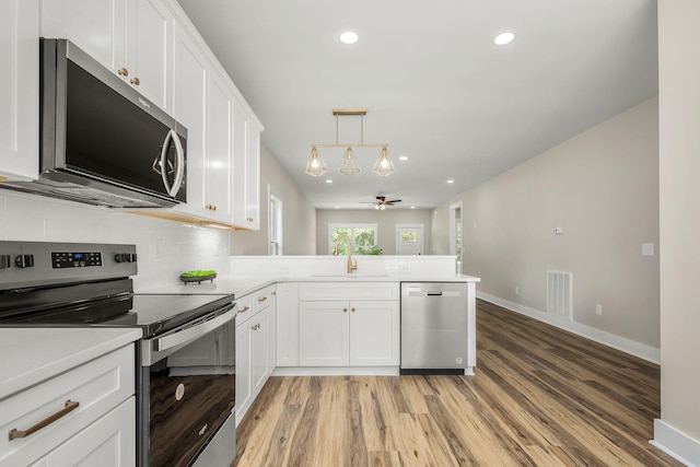 223 Patriot Ln, Estill Springs, TN 37330 - kitchen featuring stainless steel appliances, a peninsula, white cabinets, light wood finished floors, and tasteful backsplash