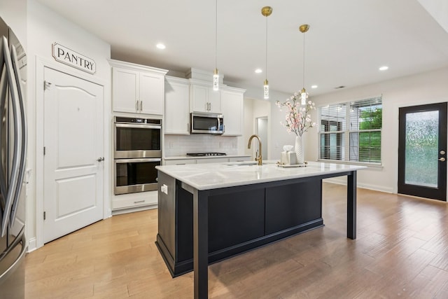 6807 Kew Gdn, Smyrna, TN 37167 - kitchen with stainless steel appliances, white cabinetry, light wood-style flooring, tasteful backsplash, and a kitchen island with sink