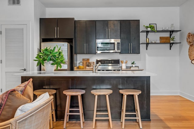 201 S 11th St, Nashville, TN 37206 - kitchen with appliances with stainless steel finishes, a kitchen bar, light wood-style flooring, a kitchen island with sink, and open shelves