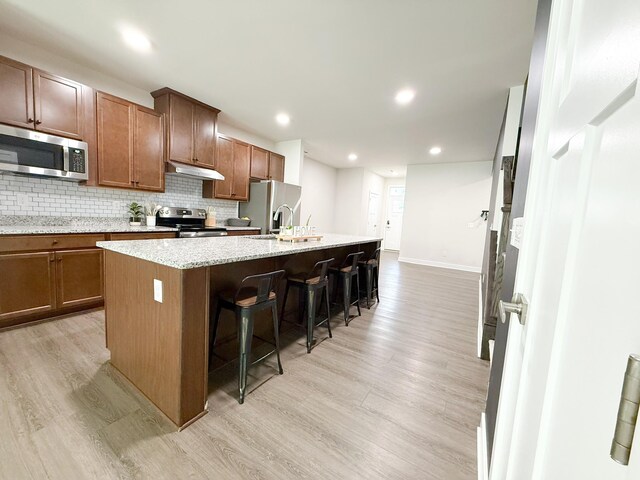 101 Percheron Pl, Smyrna, TN 37167 - kitchen featuring stainless steel appliances, under cabinet range hood, light wood-style floors, a breakfast bar, and an island with sink