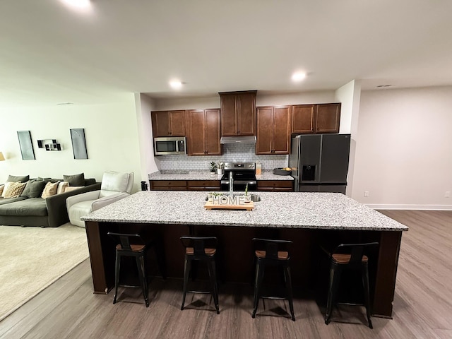 101 Percheron Pl, Smyrna, TN 37167 - kitchen featuring stainless steel appliances, dark wood-style floors, a center island with sink, decorative backsplash, and a kitchen bar
