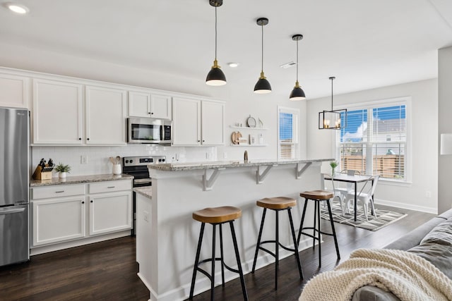 9007 Outpost Dr, Spring Hill, TN 37174 - kitchen featuring appliances with stainless steel finishes, white cabinets, dark wood-style flooring, a kitchen bar, and decorative backsplash