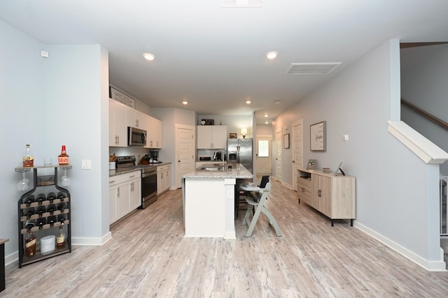 2004 Hardwick Ln, Gallatin, TN 37066 - kitchen with appliances with stainless steel finishes, a kitchen bar, light wood-type flooring, a center island with sink, and white cabinetry