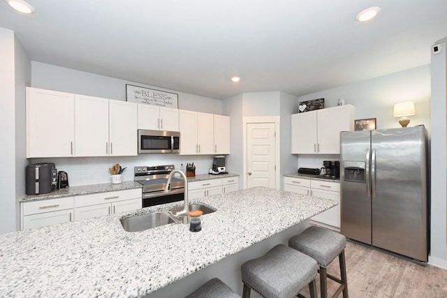 2004 Hardwick Ln, Gallatin, TN 37066 - kitchen with stainless steel appliances, a kitchen breakfast bar, white cabinetry, light wood-style flooring, and light stone countertops